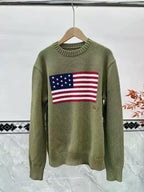 Green sweater with American flag design on a hanger against a white wall.