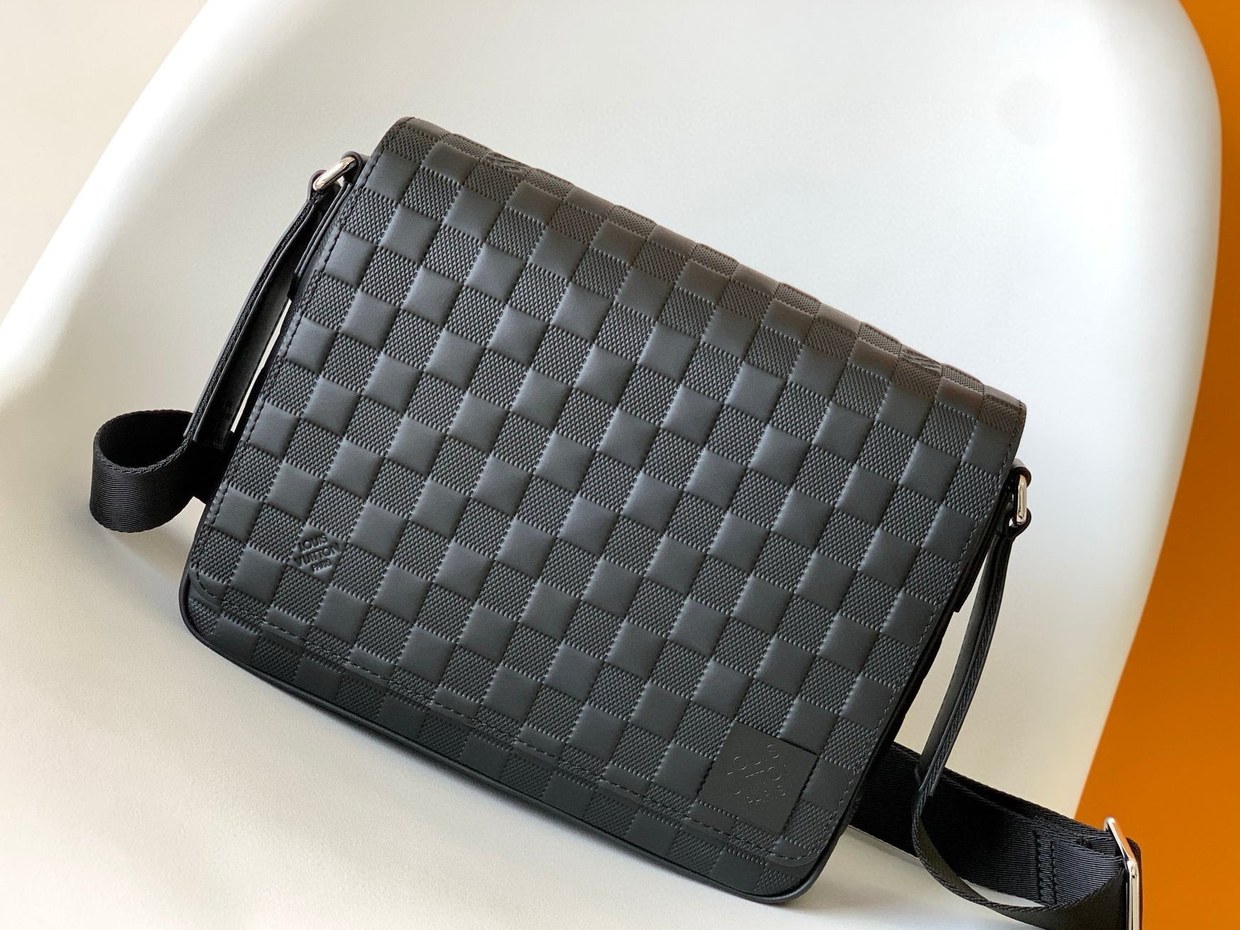 Black woven leather bag on a white surface with an orange background