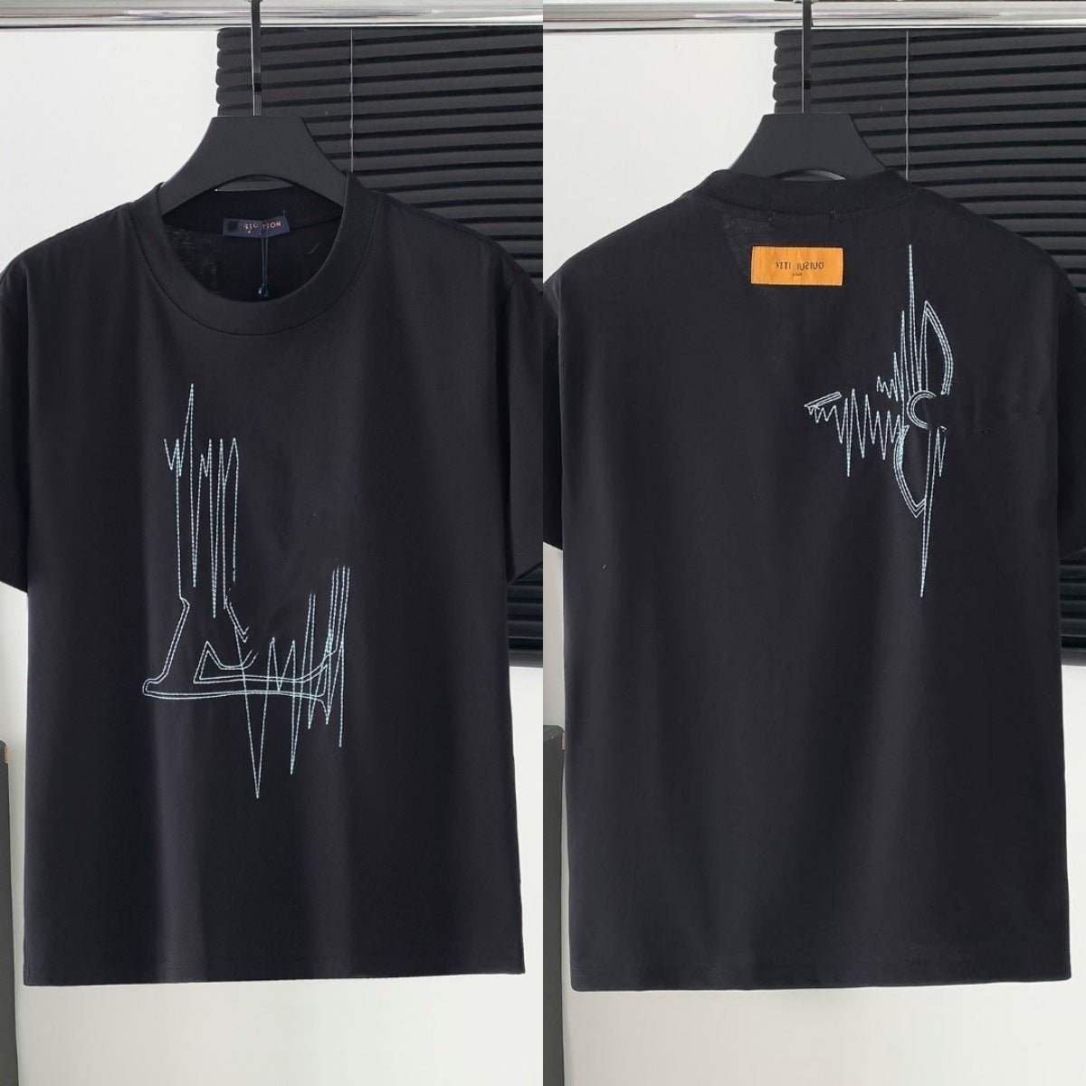 Black t-shirt with white graphic design on a hanger against a neutral background